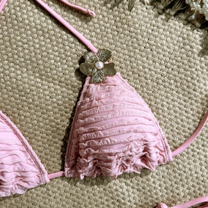 Close-up of pink pleated bikini top featuring golden metal flower with pearl detail