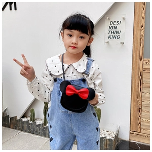 Detail of a black circular crossbody bag with a 3D red bow and white polka dot shirt