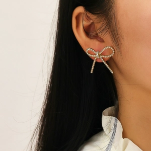 Close-up detail of a sparkling gold bow earring with crystals worn by a model