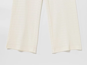 Dettaglio dei pantaloni larghi crema con trama a onde e finitura dell'orlo pieghettato