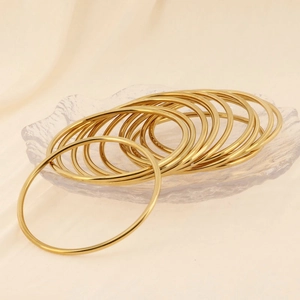 Close-up of stackable 18K gold plated minimalist thin bangles on fabric and glass