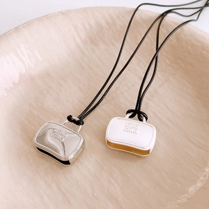 Detail of mini handbag pendants with letter logo on minimalist black cord necklaces