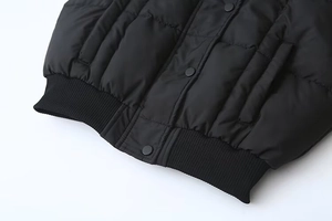 Dettaglio gilet trapuntato nero con bordo a coste e bottoni automatici in metallo