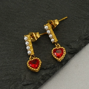 Elegante Goldohrringe mit herzförmigen roten Steinen und Perlenakzenten auf Steinhintergrund