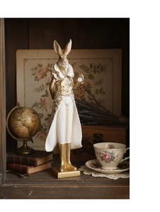 Close-up of resin rabbit in white gown with gold embroidery on a vintage bookshelf