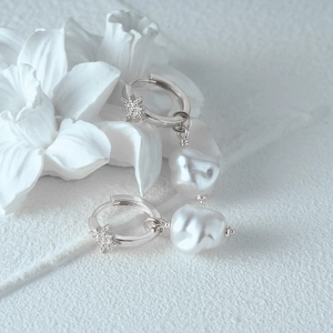 Detailed shot of S925 silver star earrings with baroque pearls on a white lily background