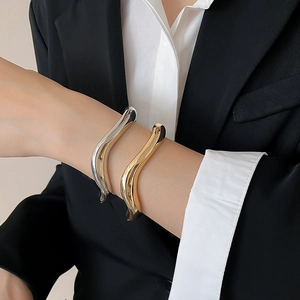 Close-up of minimalist gold and silver wavy open bangles worn with professional attire
