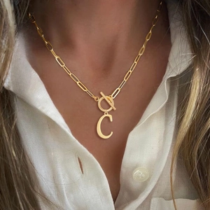 Close-up of golden paperclip chain necklace with T-bar clasp and letter C pendant