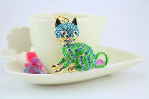 Detail of metal lucky cat keychain with blue and green rhinestones on a white cup