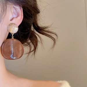 Close-up of model wearing gold circular studs with amber brown resin pendant earrings