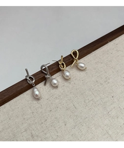 Detail of knotted gold and silver earrings with pearls hanging on a wooden beam