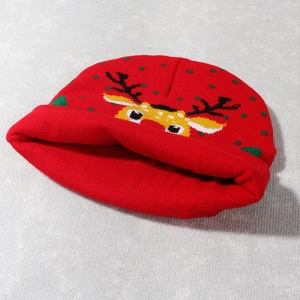 Close-up of a red knitted Christmas beanie with a reindeer pattern and green dots