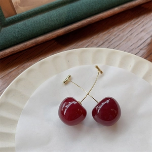 Retro red cherry drop earrings with gold stems on a decorative white ceramic plate