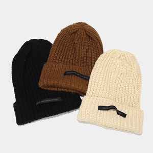 Primer plano de gorros de punto grueso en negro, marrón y beige con etiquetas textiles