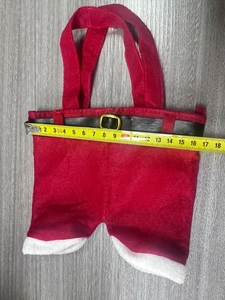 Détail du sac cadeau de Noël en forme de pantalon rouge avec mesure de largeur de 15 cm