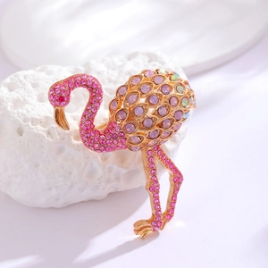 Detail of pink crystal flamingo brooch with gold plating on a textured white stone