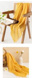 Detail of yellow cotton linen scarf with fringe edges draped over a wooden chair