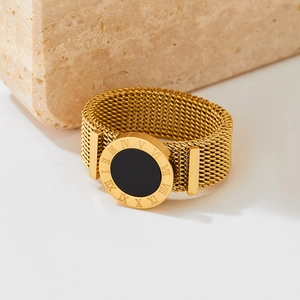 Golden mesh band ring with Roman numerals and black circular face on textured stone