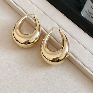 Macro detail of polished golden teardrop earrings on a beige velvet background