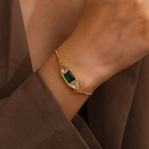 Gros plan du bracelet chaîne serpent dorée avec pierres précieuses vert émeraude et claires