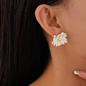 Close-up of a delicate white daisy earring with yellow stamen worn by a female model