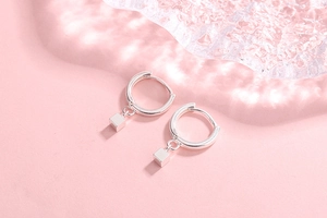 Detail view of silver square charm earrings on a soft pink background with glass decor