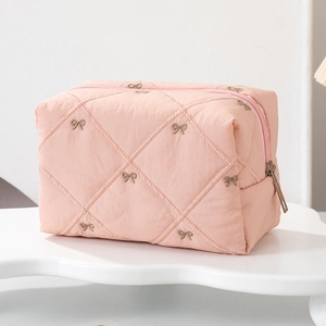 Detail of pink quilted cosmetic bag featuring ribbon embroidery and silver zipper