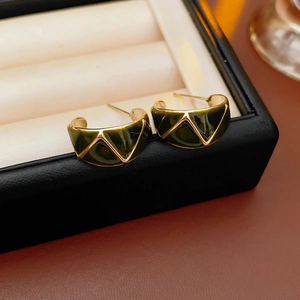 Macro shot of vintage C-shape enamel earrings with gold geometric patterns in a box