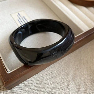 Detail of a wide black and white marble pattern acrylic bangle on a wooden jewelry box