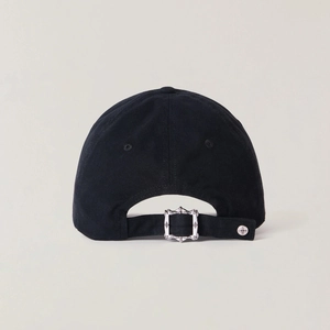 Detail of adjustable metal buckle with cross emblem on washed black cotton baseball cap
