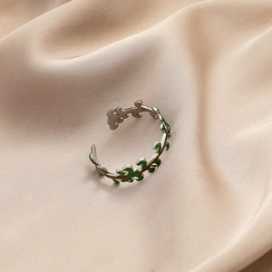 Macro detail of silver adjustable open ring with green enamel leaves on silk fabric