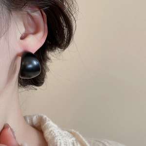 Close-up of elegant matte black C-shape stud earring worn by a model in soft lighting