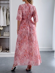 Back view of a long pink floral maxi dress with waist tie in a modern dressing room