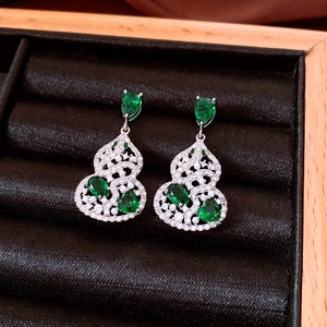 Macro shot of silver gourd earrings with green zircons and pearls on black velvet