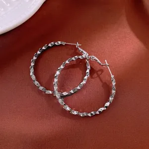 Irregular silver hoop earrings with diamond-cut texture on red silk background