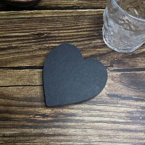 Macro view of heart-shaped natural black slate coaster on a rustic wood grain background