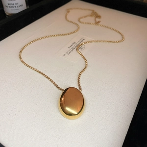 Detail of a minimalist gold oval pendant necklace resting on elegant beige fabric background