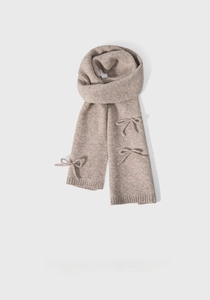 Detail shot of a beige knitted scarf with a decorative bow and soft textured weave