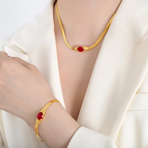 Elegant gold snake chain jewelry set with red oval gemstones on a white blazer background