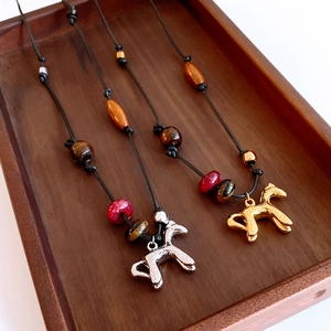Détail de pendentifs cheval or et argent avec cordons perlés sur plateau bois