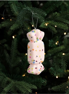 Pink candy Christmas tree ornament hanging on branch with warm festive bokeh background