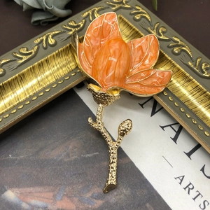 Detail of elegant orange enamel magnolia brooch on a vintage gold frame and antique book