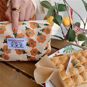 Détail d'une trousse à maquillage en velours côtelé à motif floral orange et étiquette
