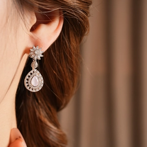 Macro detail of model wearing silver flower stud earrings with pink teardrop zircon pendants