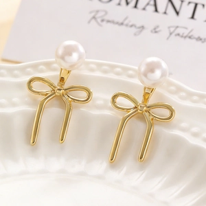 Macro shot of elegant gold bow earrings featuring high-gloss white pearls on a ceramic tray