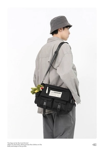 Detailed view of a black tactical messenger bag with plush charm on a male model