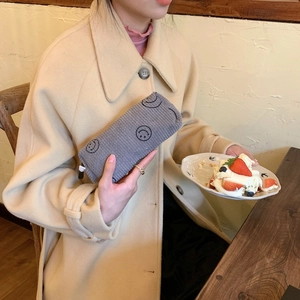Gray corduroy cosmetic bag with black smiley faces being held by a woman in a coat