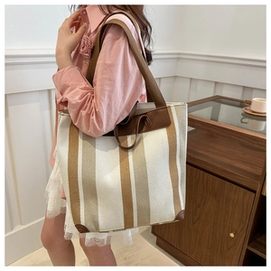 Brown striped canvas tote bag with leather trim shown on a model in a cozy interior