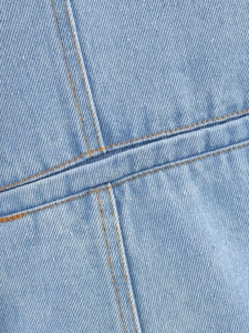 Detailed close-up of light blue twill denim fabric with contrast orange stitching