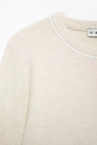 Detailed macro view of beige knit sweater neckline with fine texture and brand tag